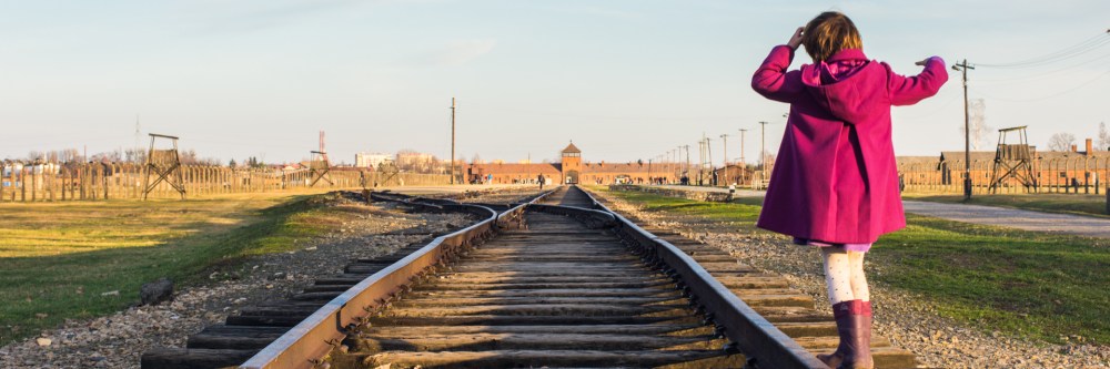A child in a purple coat plays on the train tracks at Birkenau