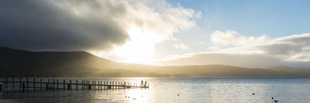 Sun setting over the water with a pier in silhouette at Bruny Island